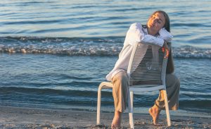 a beautiful woman sits on a chair near the sea.