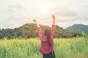 young happy woman raising hands in yellow flower field on sunset